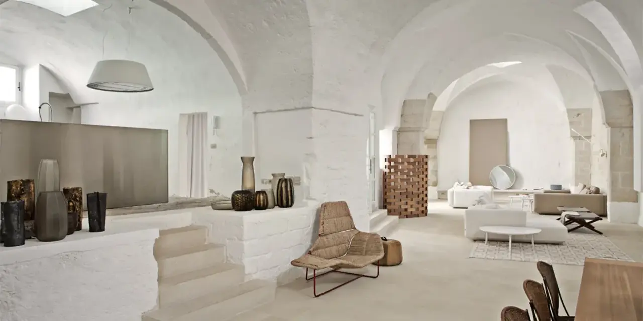 Interni moderni con soffitti a volta, un'elegante cucina a vista, zona living con divani e poltrone in vimini, e dettagli decorativi in ceramica.