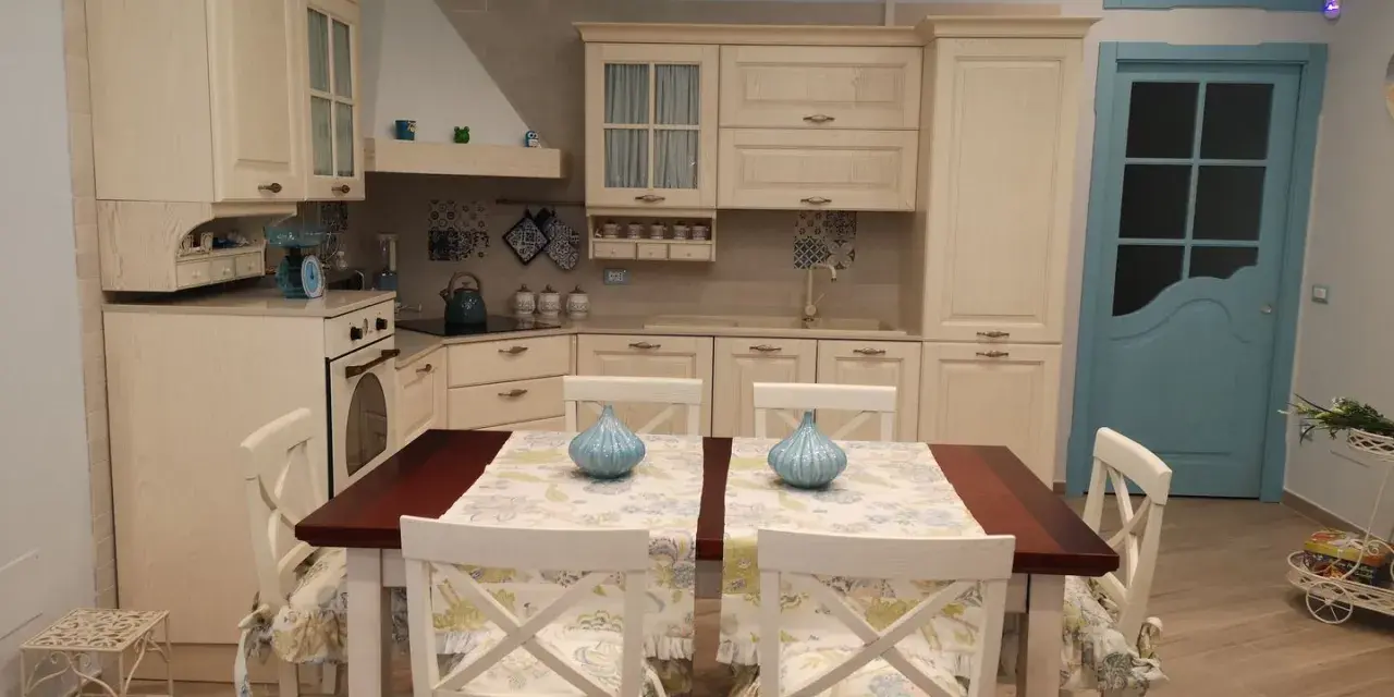 Accogliente piccola tavernetta casa con cucina in legno chiaro, tavolo da pranzo e porta azzurra.