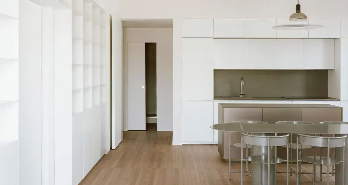 Interni moderni con cucina a isola, tavolo e sedie. Ampia libreria a muro, segno di un **cambio destinazione d'uso da magazzino ad abitazione**.