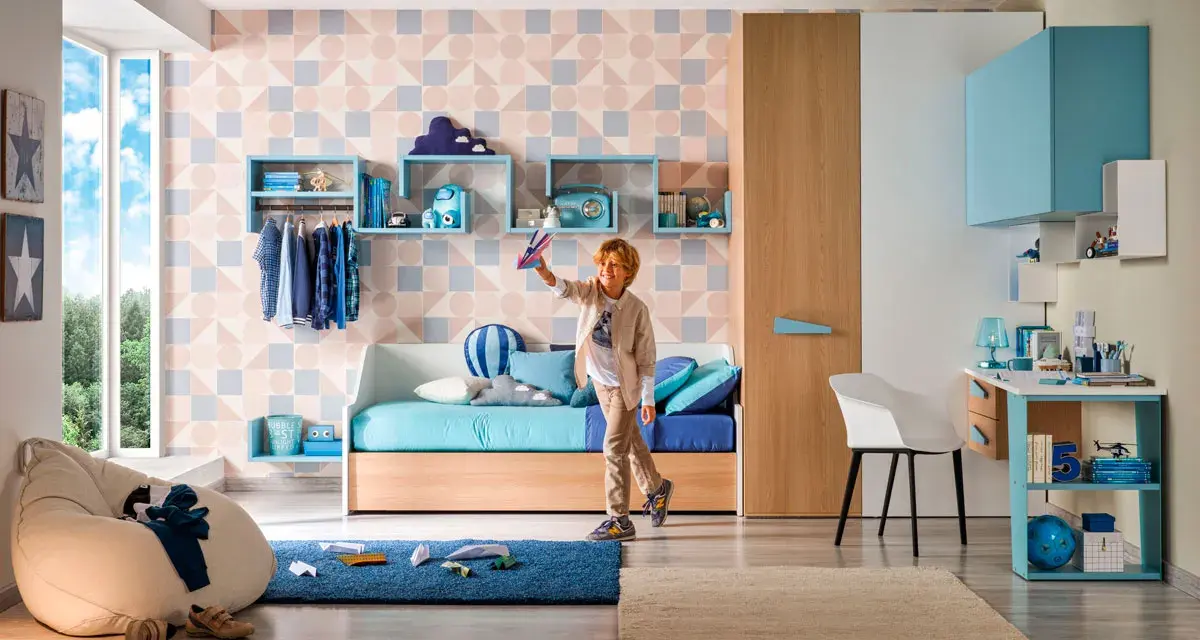 Ragazzo gioca con aeroplanino in cameretta. Ecco come sistemare i libri senza libreria: mensole a muro e contenitori colorati.