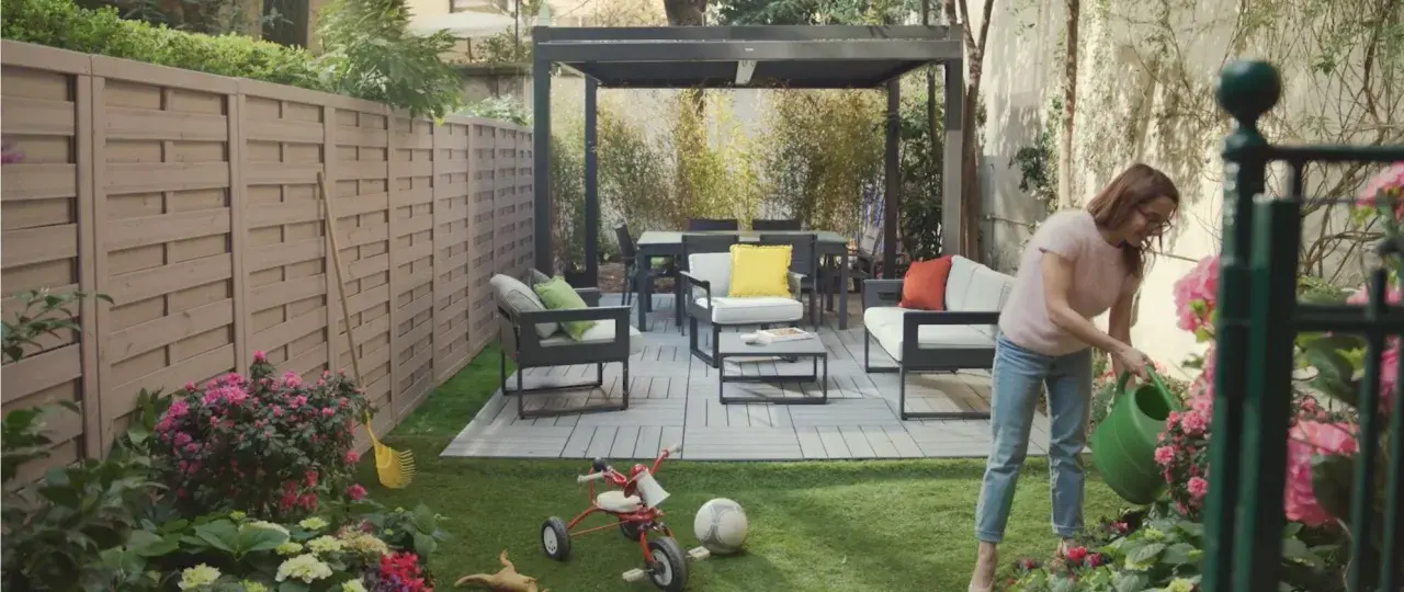 Donna annaffia fiori in un giardino con mobili moderni e un triciclo, un esempio di giardino idee originali.