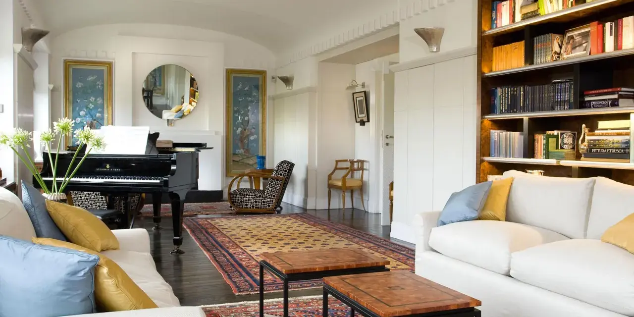 Salotto con pianoforte a coda, divani bianchi, tappeti orientali e libreria. Un perfetto esempio di arredamento classico moderno.