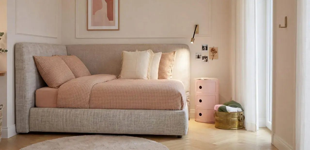 Un angolo letto con biancheria a quadri, cuscini morbidi e un quadro astratto. L'ambiente è accogliente, perfetto per creare camere aesthetic.