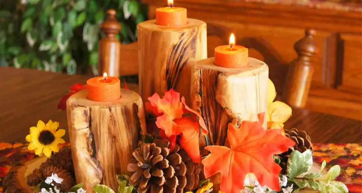 Un semplice centrotavola autunnale con tronchi di legno, candele arancioni, pigne e foglie colorate.