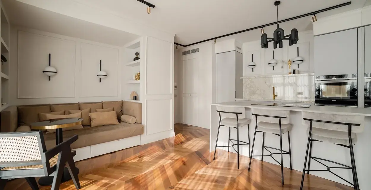Open space con ingresso aperto su soggiorno. Divano angolare, bancone cucina con sgabelli e parquet a spina di pesce.