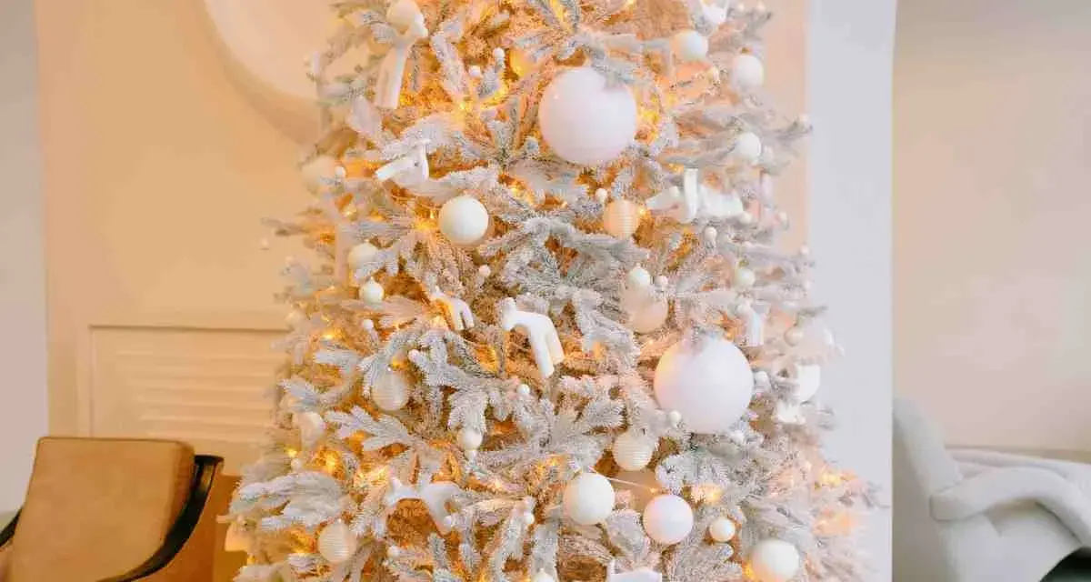 Albero di Natale innevato con luci calde, palline bianche e dorate, e decorazioni a forma di angeli e cervi. Un'elegante idea per un albero di Natale bianco e oro.