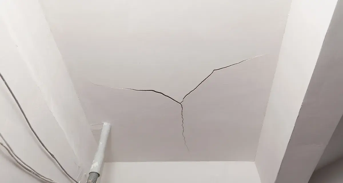 Crepe sul soffitto, un segno che il tempo o un problema strutturale sta lasciando il suo segno. Cavi elettrici e un tubo corrono lungo il muro.