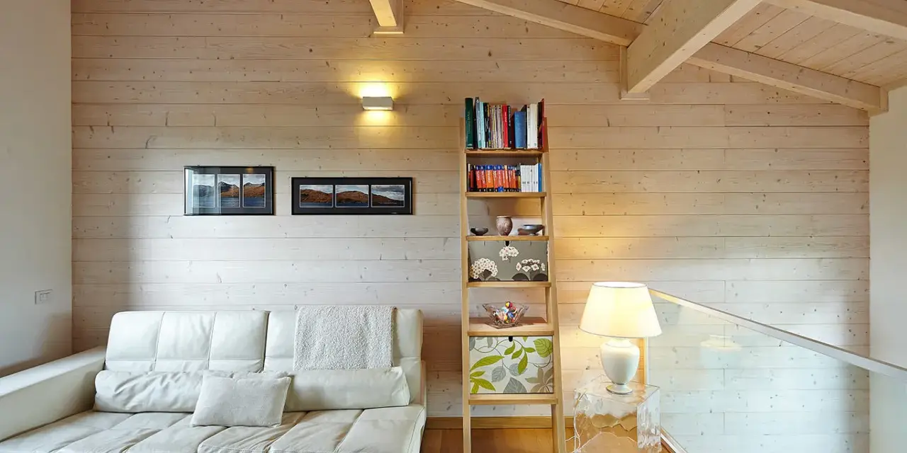 Soggiorno accogliente con divano bianco, libreria a giorno e un suggestivo tetto in legno a vista.