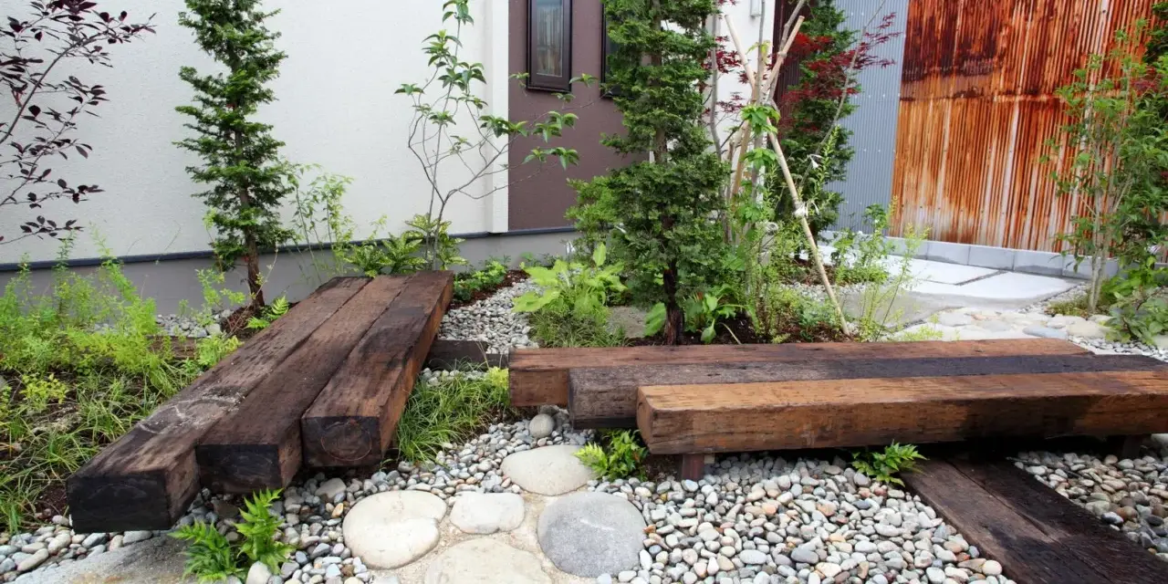 Un piccolo giardino zen con panchine in legno riciclato, ghiaia e piante verdi. Perfetto per idee giardino piccolo fai da te.