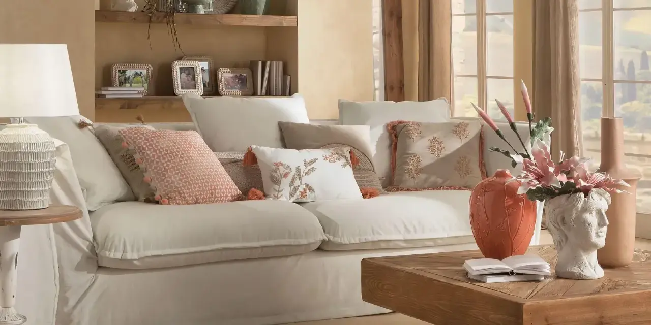 Divano bianco con cuscini decorati, lampada e tavolino in legno creano un'atmosfera di **stile cozy**.