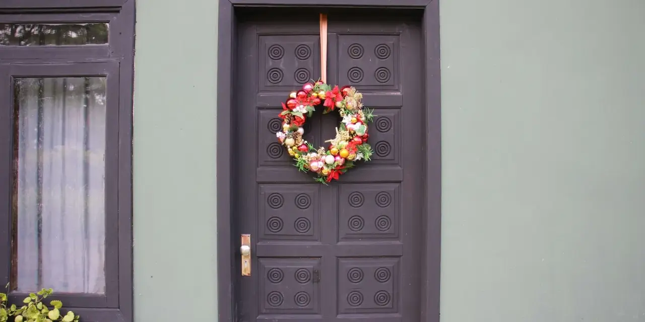 Ghirlanda natalizia appesa con un nastro alla porta scura, un esempio di come appendere la ghirlanda alla porta per le feste.