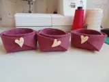 Tre cestini in feltro fai da te, color melanzana, decorati con bottoni a forma di cuore. Perfetti per organizzare piccoli oggetti.