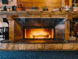 Camino in pietra e legno, con fuoco acceso, che evoca idee camini rustici di montagna. Sopra, oggetti d'epoca e legna accatastata.