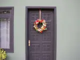 Ghirlanda natalizia appesa con un nastro alla porta scura, un esempio di come appendere la ghirlanda alla porta per le feste.