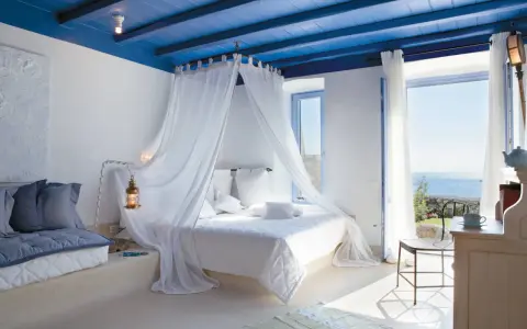 Camera da letto stile mediterraneo con soffitto blu, letto a baldacchino bianco e vista mare.