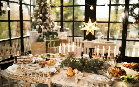 Un tavolo imbandito per Natale, con torta, arrosti e candele. Un modo perfetto per come addobbare la cucina per Natale, con un albero illuminato sullo sfondo.