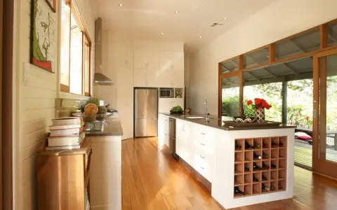 Cucina moderna con isola centrale dotata di una cantina a vista per il vino. Ampie vetrate si aprono su un patio esterno.