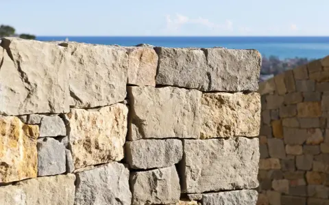 Muro a secco per contenimento terra, con vista sul mare e un borgo in lontananza.