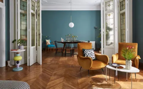 Salotto con poltrone ocra, tavolino dal design moderno e porte a soffietto con vetri decorati, un mix di stile vintage e contemporaneo.