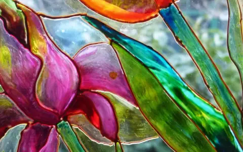 Dettaglio di un fiore dipinto su vetro, con petali viola e verdi vibranti. Un'ispirazione per il **dipinto su vetro fai da te**.