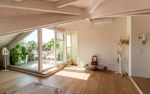 Luminoso sottotetto con travi a vista e un terrazzo fiorito. Idee sottotetto molto basso per sfruttare ogni angolo.