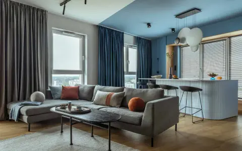 Soggiorno moderno con divano grigio, tavolino nero e tende blu e grigie. Un esempio di come scegliere le tende per il salotto per un look sofisticato.
