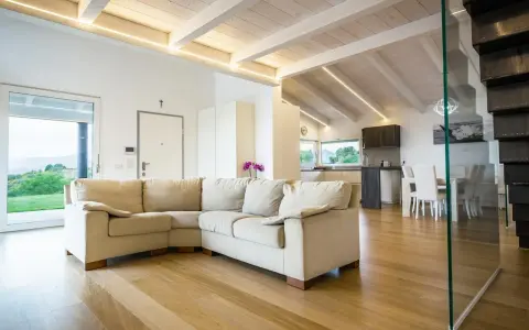 Soggiorno moderno con travi in legno sbiancate senza carteggiare, divano beige e cucina a vista.