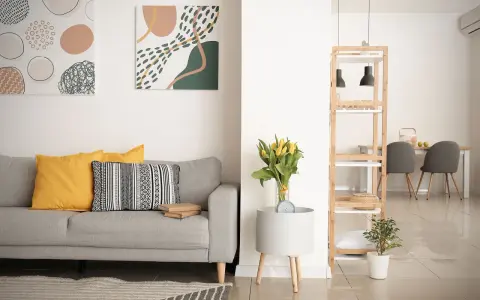 Soggiorno moderno con divano grigio, cuscini gialli e decorazioni astratte. Si nota la differenza tra ammobiliato e arredato: qui, ogni elemento è scelto con cura per creare un ambiente accogliente.