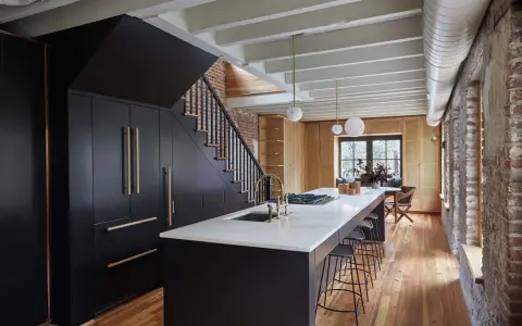 Cucina moderna con isola centrale, bancone in marmo e sgabelli. Armadi neri sotto la scala, con maniglie in legno. Soffitto con travi a vista e tubi. Pareti in mattoni a vista. La **taverna** ha un'**altezza** di circa **2,40** metri.