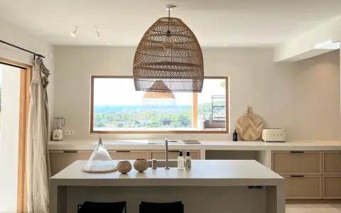 Cucina luminosa con isola centrale, lampadario in rattan e vista mare. Arredamento in stile casa bohemien con materiali naturali.