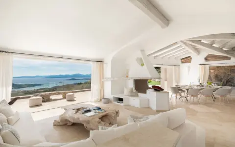Soggiorno luminoso con vista mare, perfetto per l'arredo case al mare. Divani bianchi, camino moderno e tavolo da pranzo per godersi il panorama.