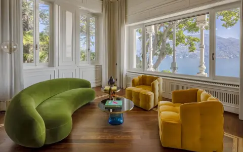 Un salotto con divano verde curvo e poltrone gialle, tavolini rotondi e vista lago. Un perfetto esempio di **art deco arredamento** con tocchi moderni.