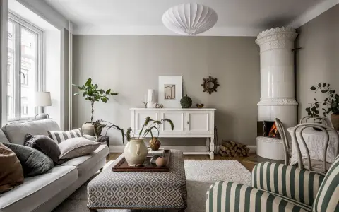Salotto accogliente con camino in maiolica, divano grigio e pouf decorato. L'arredamento stile classico si fonde con elementi moderni.