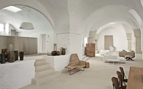 Interni moderni con soffitti a volta, un'elegante cucina a vista, zona living con divani e poltrone in vimini, e dettagli decorativi in ceramica.