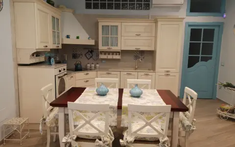 Accogliente piccola tavernetta casa con cucina in legno chiaro, tavolo da pranzo e porta azzurra.