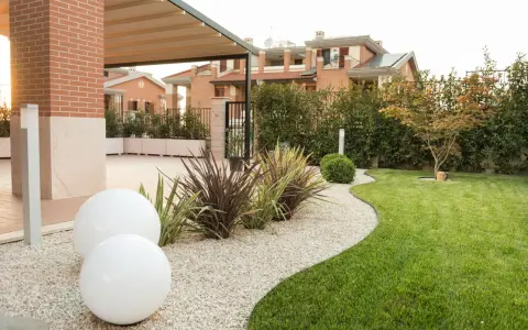 Giardino moderno con ghiaia bianca, sfere luminose e piante decorative. Belle idee giardino ingresso casa per un'accoglienza elegante.