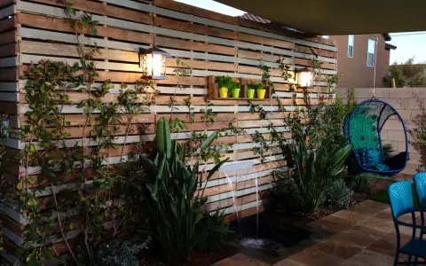 Giardino incantevole con idee creative con bancali: una parete in legno, cascata, piante rigogliose e una sedia sospesa a forma di pavone.