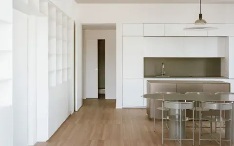 Interni moderni con cucina a isola, tavolo e sedie. Ampia libreria a muro, segno di un **cambio destinazione d'uso da magazzino ad abitazione**.