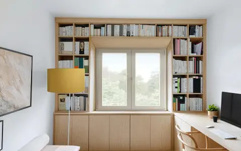 Una libreria a ponte in legno chiaro incornicia una finestra, con libri ordinati e un'area studio funzionale.