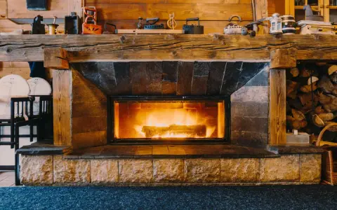 Camino in pietra e legno, con fuoco acceso, che evoca idee camini rustici di montagna. Sopra, oggetti d'epoca e legna accatastata.