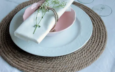 Sottopiatti in stoffa fai da te, con tovagliolo bianco legato da spago e decorato con un rametto fiorito.