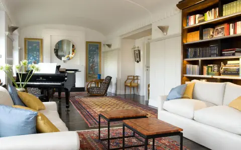 Salotto con pianoforte a coda, divani bianchi, tappeti orientali e libreria. Un perfetto esempio di arredamento classico moderno.