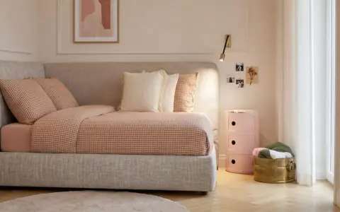 Un angolo letto con biancheria a quadri, cuscini morbidi e un quadro astratto. L'ambiente è accogliente, perfetto per creare camere aesthetic.