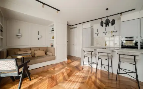 Open space con ingresso aperto su soggiorno. Divano angolare, bancone cucina con sgabelli e parquet a spina di pesce.
