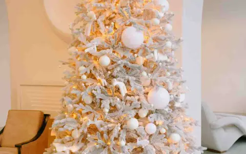 Albero di Natale innevato con luci calde, palline bianche e dorate, e decorazioni a forma di angeli e cervi. Un'elegante idea per un albero di Natale bianco e oro.