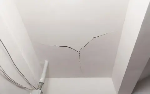 Crepe sul soffitto, un segno che il tempo o un problema strutturale sta lasciando il suo segno. Cavi elettrici e un tubo corrono lungo il muro.