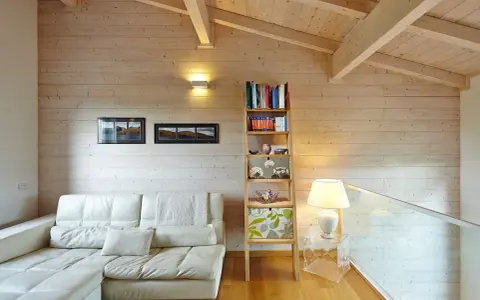 Soggiorno accogliente con divano bianco, libreria a giorno e un suggestivo tetto in legno a vista.