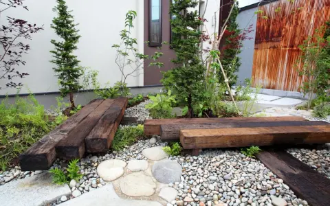Un piccolo giardino zen con panchine in legno riciclato, ghiaia e piante verdi. Perfetto per idee giardino piccolo fai da te.