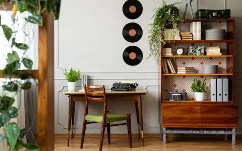 Scrivania con macchina da scrivere e sedia verde, libreria con dischi in vinile e piante. Perfette idee arredamento vintage per un angolo studio.