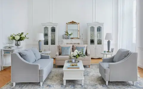 Salotto luminoso in stile shabby chic contemporaneo, con divani grigi, mobili bianchi e dettagli dorati.